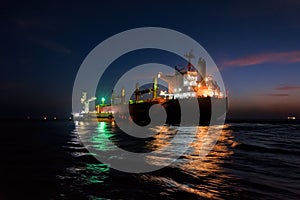Night loading big mother sea bulk carrier ship with Bauxite aluminium ore from the mini bulk carrier feeder vessel at offshore