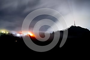 Night long exposure shot showing fog and clouds rolling over mountains with blue and orange lights of village in