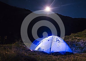 Night mountain landscape with illuminated blue tent. Mountain peaks and the moon. outdoor at Lacul Balea Lake, Transfagarasan,