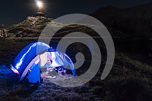 Night mountain landscape with illuminated blue tent. Mountain peaks and the moon. outdoor at Lacul Balea Lake, Transfagarasan,