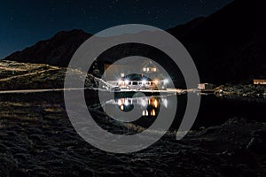 Night mountain landscape with illuminated blue tent. Mountain peaks and the moon. outdoor at Lacul Balea Lake, Transfagarasan,