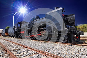 At night, the old steam locomotive is illuminated by modern street lights.