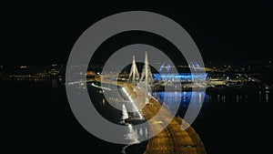 Night panoramic view on city skyscraper, car traffic on bridge and sport stadium