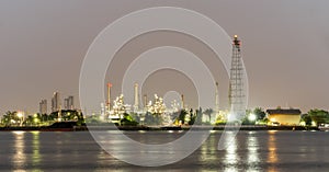 Night photo crude oil refinery plant and many chimney with petrochemical tanker or cargo ship at coast of the river with colorful