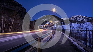 Night photo of illuminated Soldeu village. Car light streaks or patterns on road.