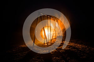 Night photo of metal swing standing outdoor at night time with fog and surreal toned light on background. Nobody there.