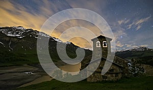 Night photography of a landscape of the Alps. Lake with stars in the sky and moving clouds. Church in the mountain