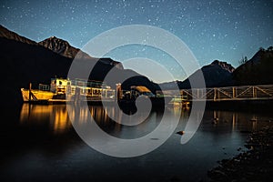 Night pier at mountain lake with tourist boat at night with stars in the sky