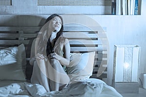 Night portrait of young beautiful depressed and sad Asian Chinese woman having insomnia sitting in bed sleepless suffering anxiety