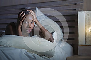 Night portrait of young scared and stressed black african American woman on bed upset unable to sleep suffering hangover headache