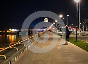 night promenade at sea side blue  starry sky and full moon  street lantern  blurred light at sea water people silhouette  walk an