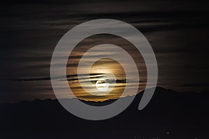 Night scene - full moon shining brightly in sky with clouds on mountains background.