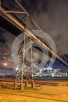 Night scene with illuminated petrochemical production plant and pipeline overpass,