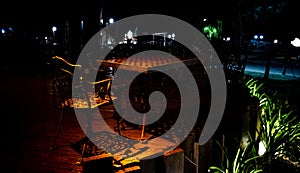 Night scene of an isolated chair and table on a wooden deck of an elegant outdoor bar dimly lit by lamps