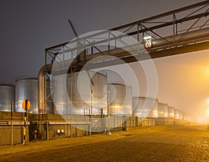 Night scene with large silo and pipeline overpass at petrochemical production plant