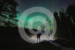 Night scene, nature of Estonia. Silhouette of a man with a flashlight in a forest with a starry sky and northern lights