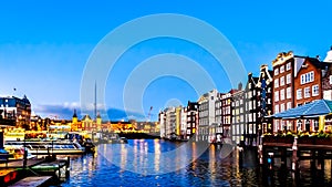 Night scene of the row of historic houses along the Damrak canal, dating back to the 18th century, in the center of Amsterdam