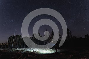 Night scene, silhouette of a man with a headlamp in the forest under the starry sky