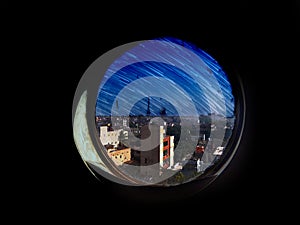 Night scene of star trails and the city seen through the circular window from dark room.