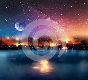 Night sea  starry sky  in harbor ,blue sea water  nebula and big moon on sea on horizon city light blurred light