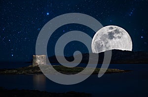 Night seascape in Sardinia with tower on the coast in La Pelosa Beach, in Stintino, with starry sky and super moon