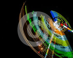 Night shot of a carnival ride in motion with fireworks