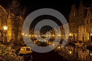 A night shot from the old bridge The Kerkbrug on the Oude Rijn with numerous boats and illuminated old canal-side houses, Leiden