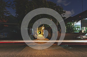 Night shot of a typical street of a city in the Philippines with lights from lamp post and homes. A single light trail of a car li