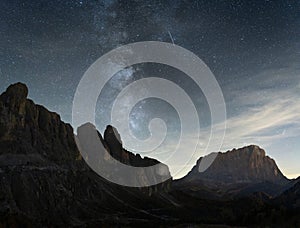 Night sky full of stars and Milky Way over desert like alpine landscape with prominent peaks, Italy