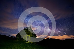 Night sky full of stars with some clouds and the milky way galaxy and an old rustic barn house in the foreground