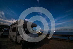 Night sky at Monte Argentario peninsula, Tuscany, Italy. Stars over camper van illuminated by moon light. Giglio Island in the