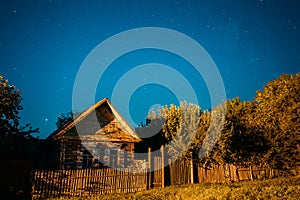 Night sky over old house in village. Night starry sky above house with bright stars and meteoric track trail. Glowing