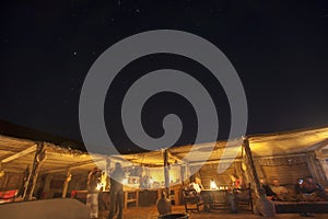 Night sky and tourists socializing in straw huts at night in Wahiba sands, Oman