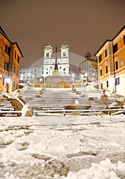 Night snowfall on empty Spanish square and steps in Rome with church Trinita di Monti in background, Italy. Piazza di Spagna