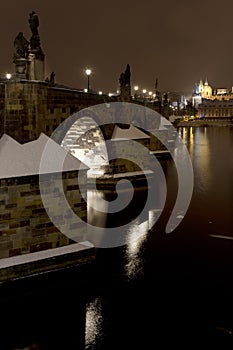 Night snowy colorful Prague Lesser Town with gothic Castle, St. Nicholas` Cathedral from Charles Bridge, Czech republic