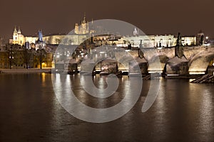 Night snowy colorful Prague Lesser Town with gothic Castle, St. Nicholas` Cathedral and Charles Bridge, Czech republic