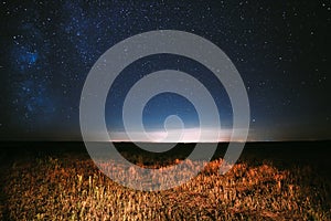 Night Starry Sky Above Field And Yellow City Lights On Background. Night View Of Natural Glowing Stars