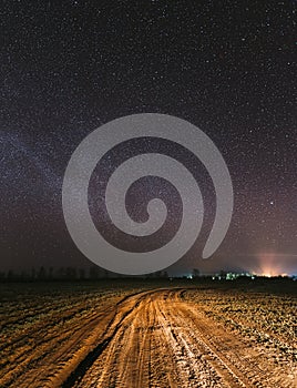 Night Starry Sky With Glowing Stars Above Countryside Road Landscape. Milky Way Galaxy And Rural Field Meadow