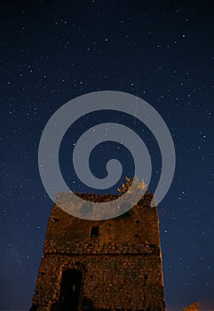 Night starry sky over an abandoned stone tower. A falling star is visible. A deep dark night.