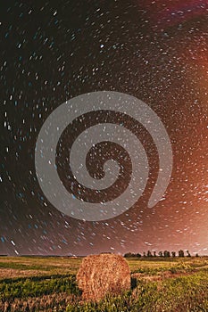 Night Starry Sky in rotation Above Country Field Meadow With Hay Bale After Harvest. Glowing Stars Above Rural Landscape