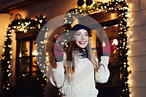 Night street portrait of young beautiful woman acting thrilled, wearing stylish knitted clothes. Model expressing joy