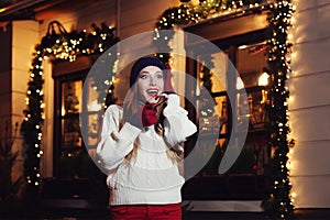 Night street portrait of young beautiful woman acting thrilled, wearing stylish knitted clothes. Model expressing joy