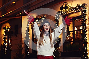 Night street portrait of young beautiful woman acting thrilled, wearing stylish knitted clothes. Model expressing joy