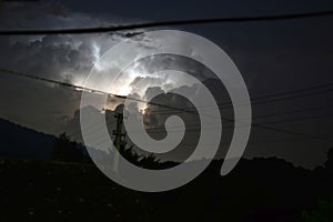 Night thunderstorm, distant illuminated cumulonimbus cloud and cloudy sky, power lines, power pole