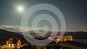 Night Time Lapse with Moon, Stars, Clouds, Mountains and Village near the Lake