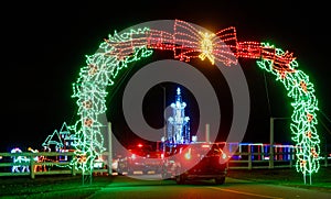 night time light show cars entering entrance under green and red trestle for Christmas