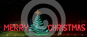 night time lights show Merry Christmas spelled out in red lights and green lights tree