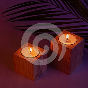 Night tropical atmosphere for vacation and relaxation with burning candles and pal leaf in purple orange sunset light, square.