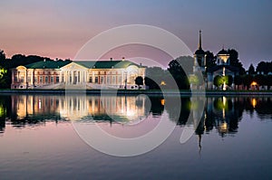 Night view of the aristocratic mansion and church with bell tower next to the pond in museum-estate Kuskovo, Moscow.