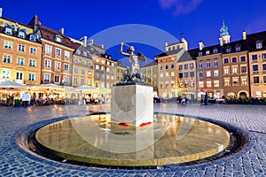 Night view of the bronze statue of Mermaid on the Old Town Market Square of Warsaw, surrounded by colorful old houses.